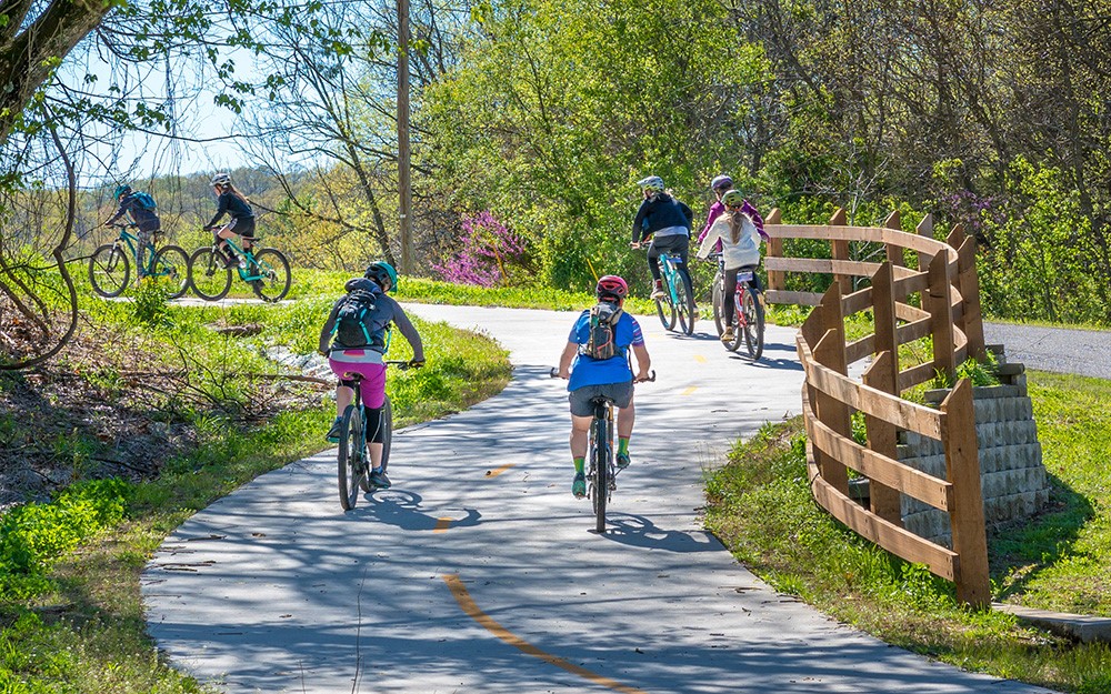 Cyclists riding through woods on paved bike trail